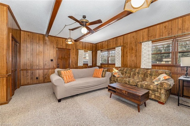 carpeted living room featuring beam ceiling, ceiling fan, wooden walls, and plenty of natural light