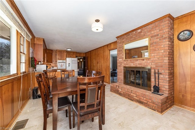 dining space with ornamental molding, wooden walls, and a brick fireplace