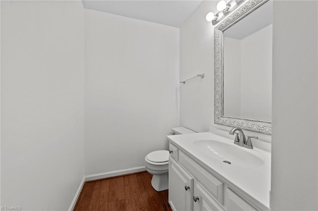 half bath featuring baseboards, wood finished floors, vanity, and toilet