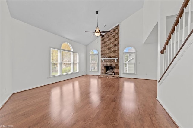unfurnished living room featuring high vaulted ceiling, a ceiling fan, stairs, wood finished floors, and baseboards
