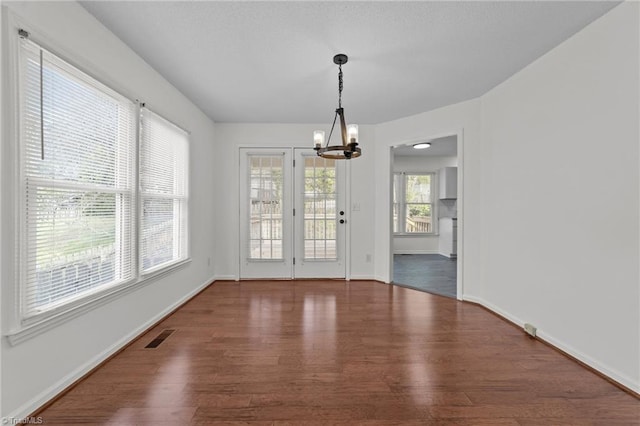 unfurnished dining area with a chandelier, wood finished floors, visible vents, and baseboards