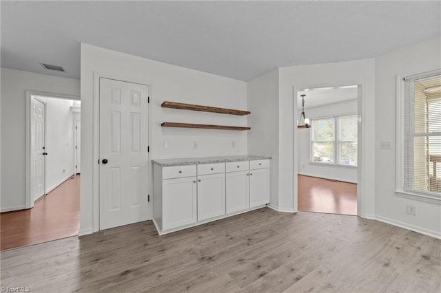 interior space with light wood-type flooring, baseboards, visible vents, white cabinetry, and open shelves