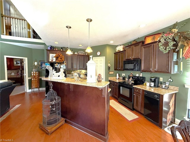 kitchen featuring black appliances, decorative light fixtures, wood finished floors, and a kitchen breakfast bar