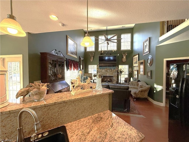 kitchen with open floor plan, a stone fireplace, a towering ceiling, a textured ceiling, and a sink