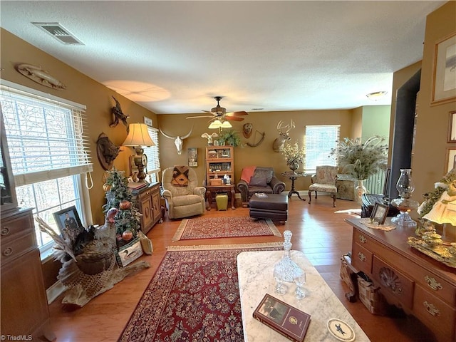 living area featuring ceiling fan, visible vents, a textured ceiling, and light wood-style flooring