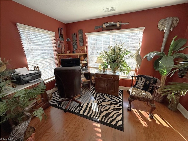 home office with a wealth of natural light, visible vents, and wood finished floors