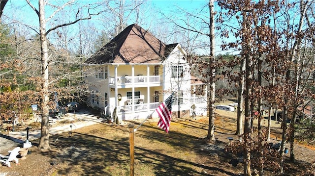 rear view of property featuring a shingled roof, a porch, stairs, a yard, and a balcony