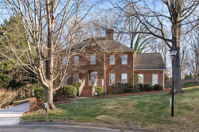 view of front of home with brick siding, a chimney, a front lawn, and roof with shingles