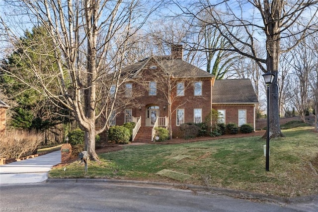 colonial-style house featuring brick siding, a chimney, and a front yard