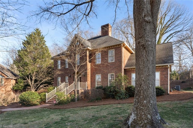 view of front facade with brick siding, a chimney, a front lawn, and roof with shingles