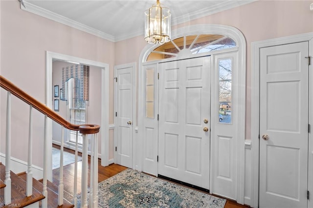 foyer entrance featuring baseboards, stairway, wood finished floors, an inviting chandelier, and crown molding