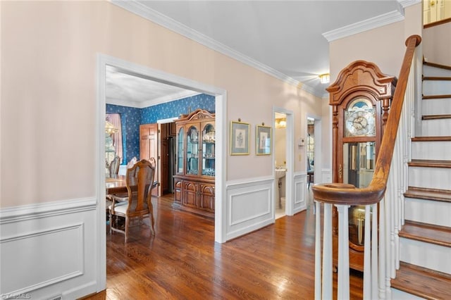 foyer entrance with wallpapered walls, wainscoting, wood finished floors, stairs, and crown molding