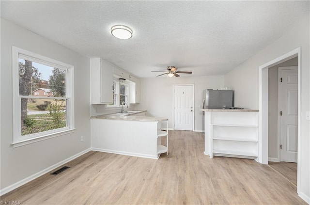 kitchen featuring white cabinetry, kitchen peninsula, a textured ceiling, and light wood-type flooring