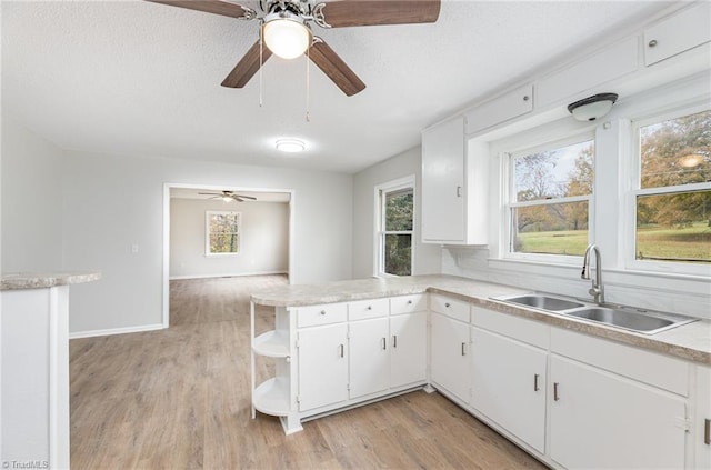 kitchen with kitchen peninsula, a textured ceiling, sink, white cabinetry, and light wood-type flooring