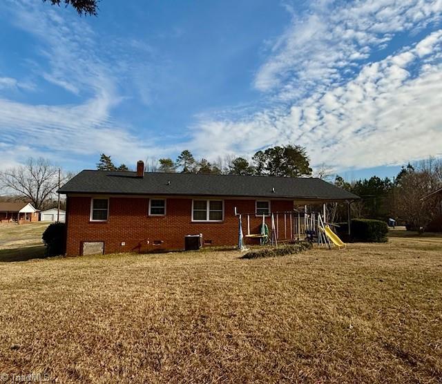 back of house featuring a playground, central AC, and a lawn