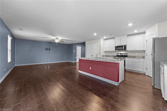 kitchen featuring stainless steel appliances, light stone countertops, a center island with sink, and white cabinets