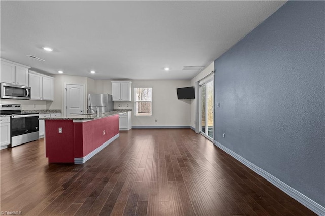 kitchen with a kitchen island with sink, stainless steel appliances, dark hardwood / wood-style floors, light stone countertops, and white cabinets