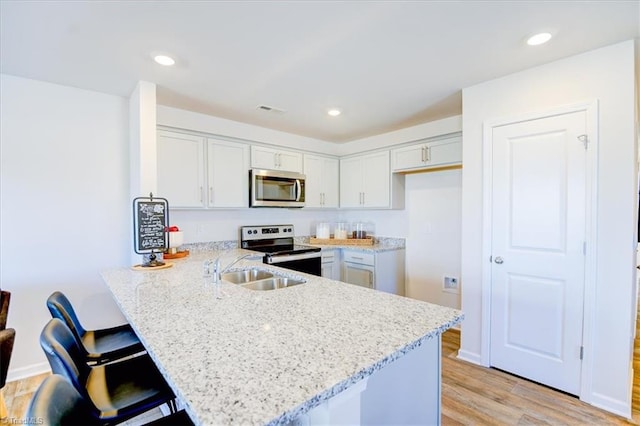 kitchen with sink, appliances with stainless steel finishes, a kitchen breakfast bar, light stone countertops, and kitchen peninsula