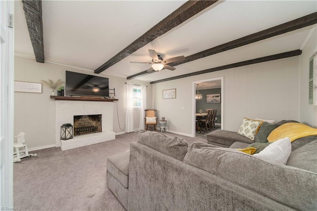 living room with ceiling fan, a brick fireplace, beamed ceiling, carpet floors, and ornamental molding