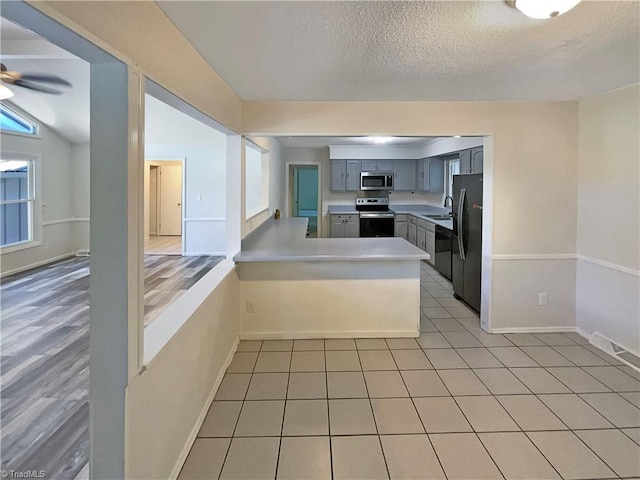 6630 Riverwood Rd, Walkertown, NC 27051 - kitchen with stainless steel appliances, gray cabinetry, a peninsula, a textured ceiling, and light countertops