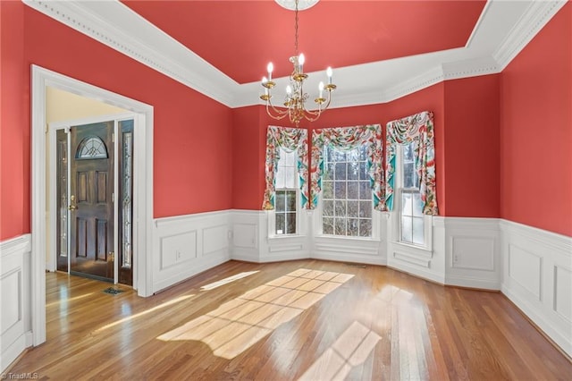 unfurnished dining area featuring a wainscoted wall, a notable chandelier, and light wood-style flooring