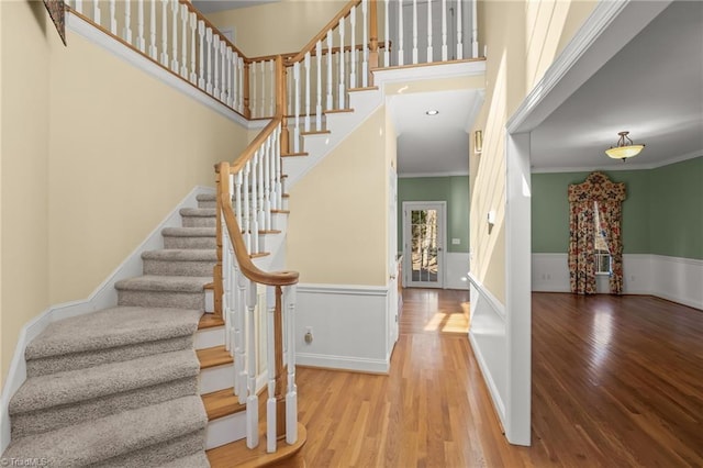 stairway with a wainscoted wall, crown molding, a high ceiling, and wood finished floors