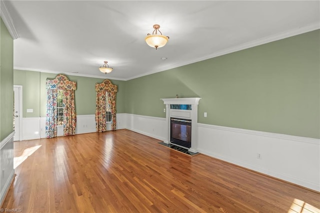 unfurnished living room featuring a fireplace with flush hearth, a wainscoted wall, ornamental molding, and wood finished floors