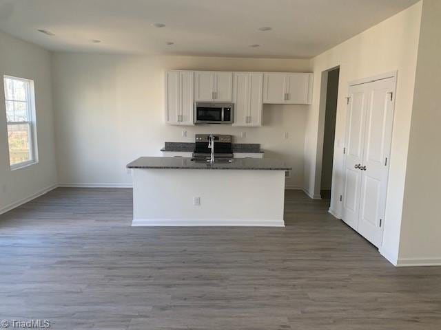 kitchen with dark hardwood / wood-style flooring, white cabinets, range, and an island with sink