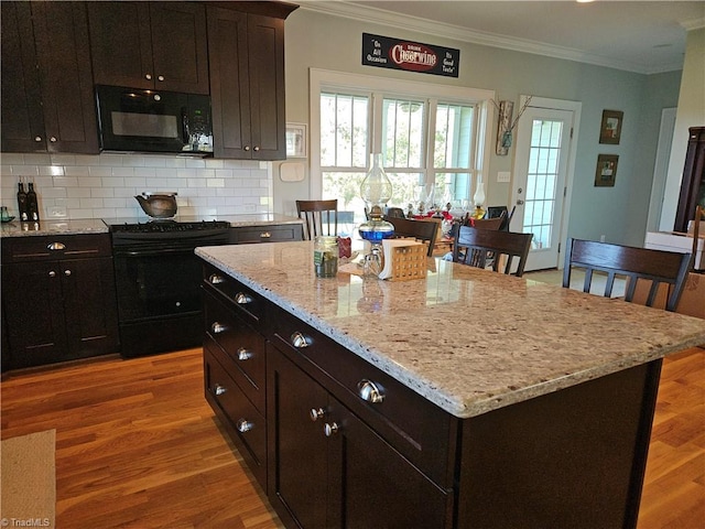 kitchen featuring ornamental molding, a center island, black appliances, and light hardwood / wood-style flooring