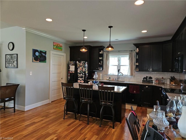 kitchen with a center island, ornamental molding, light stone countertops, pendant lighting, and light hardwood / wood-style flooring