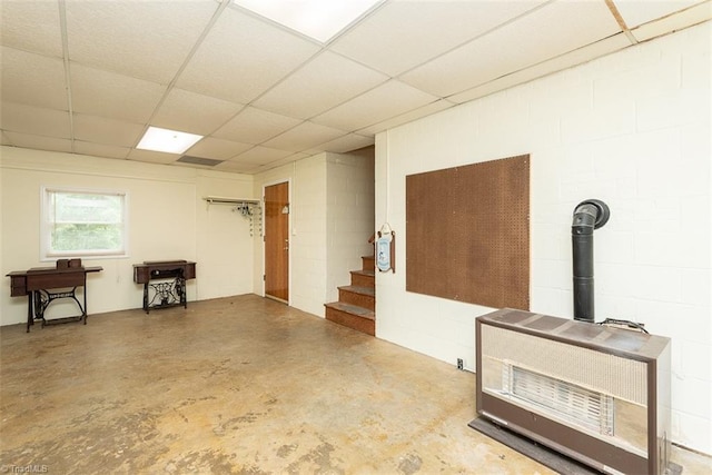 interior space featuring a wood stove, heating unit, concrete flooring, stairway, and concrete block wall