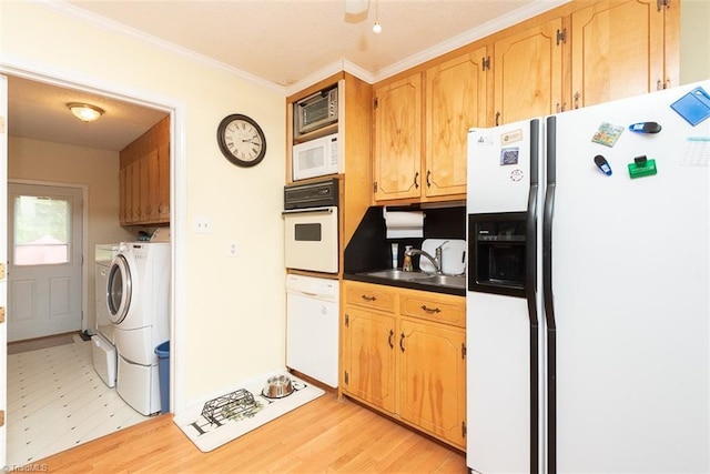 kitchen featuring washing machine and clothes dryer, dark countertops, a sink, ornamental molding, and white appliances