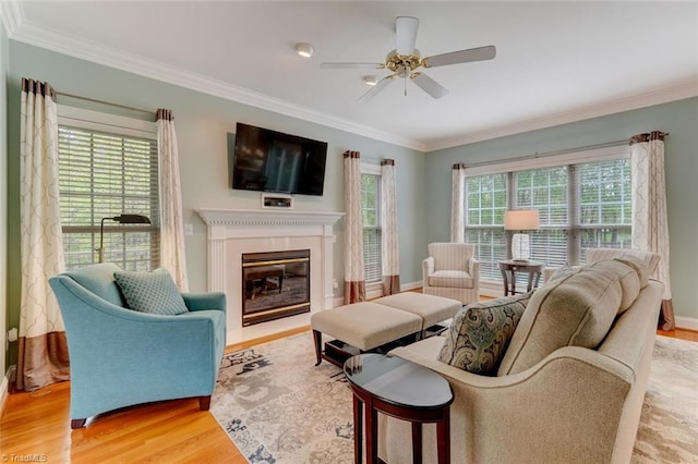 living room with a ceiling fan, baseboards, a glass covered fireplace, light wood-style floors, and ornamental molding