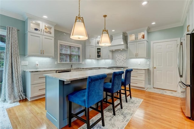 kitchen with a kitchen island, crown molding, appliances with stainless steel finishes, and custom range hood