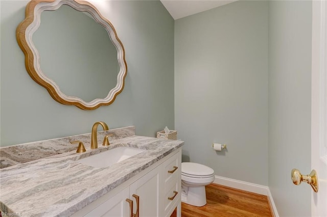 half bath featuring baseboards, vanity, toilet, and wood finished floors