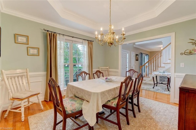 dining area featuring ornamental molding, wainscoting, stairway, a chandelier, and light wood-style flooring