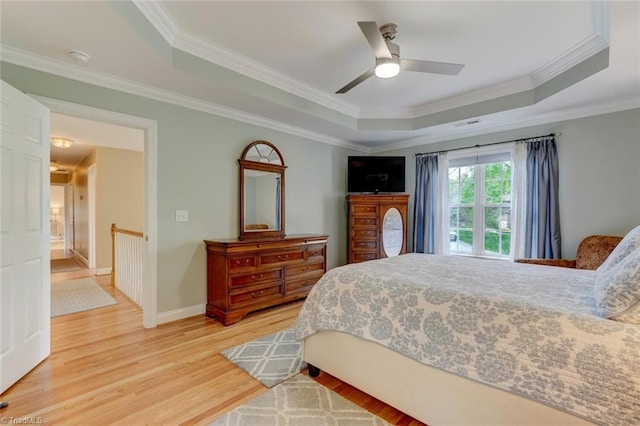 bedroom with a tray ceiling, ornamental molding, baseboards, and light wood-type flooring