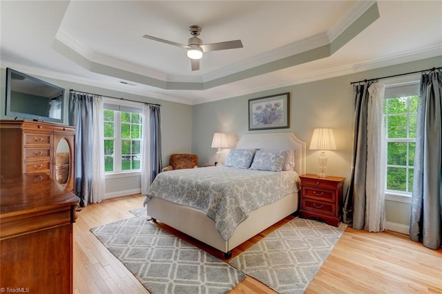 bedroom featuring crown molding, light wood finished floors, baseboards, and a tray ceiling