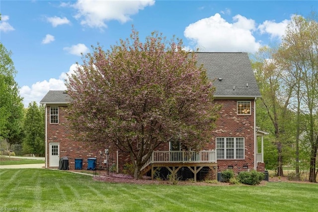 rear view of house with brick siding, a lawn, and a wooden deck