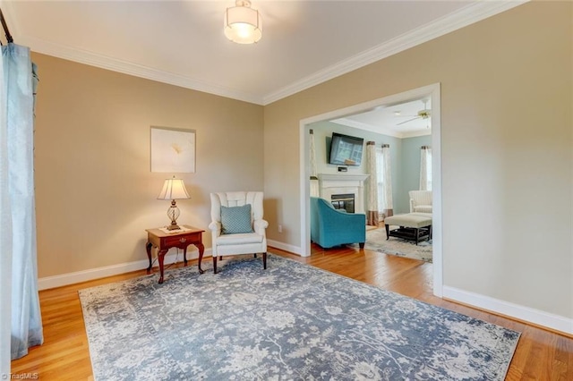sitting room featuring baseboards, a glass covered fireplace, ornamental molding, and wood finished floors