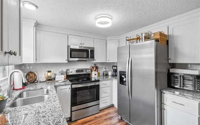 kitchen featuring light stone countertops, sink, stainless steel appliances, light hardwood / wood-style floors, and white cabinets