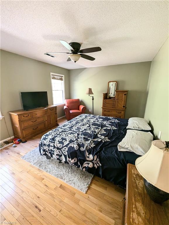 bedroom with ceiling fan, a textured ceiling, and light hardwood / wood-style flooring