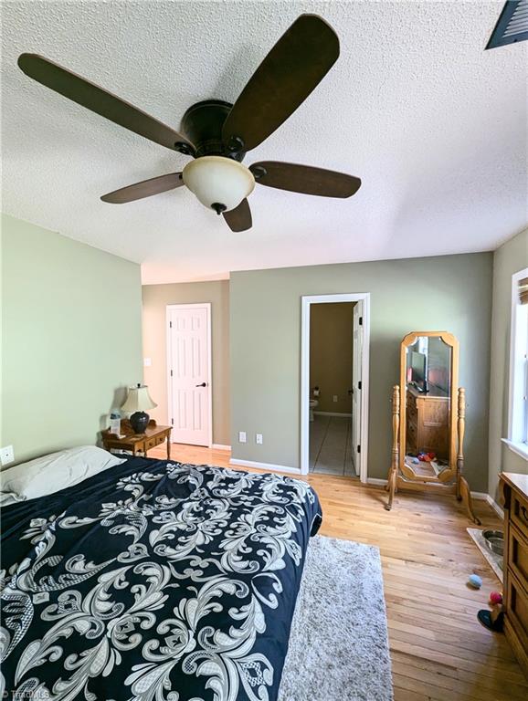 bedroom featuring light wood-type flooring, ceiling fan, connected bathroom, and a textured ceiling