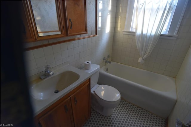 full bathroom featuring tiled shower / bath, vanity, tile walls, and toilet