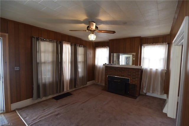 unfurnished living room with a fireplace, carpet floors, ceiling fan, and wooden walls