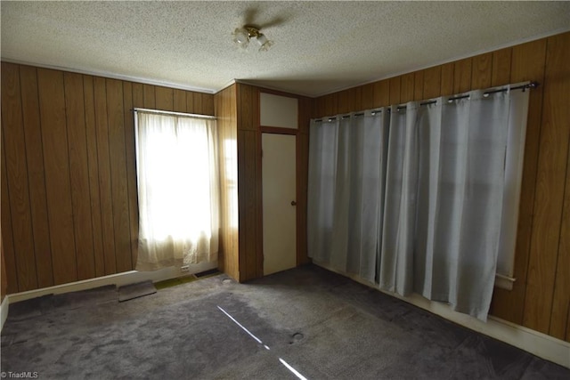 unfurnished bedroom featuring a textured ceiling, dark carpet, and wood walls