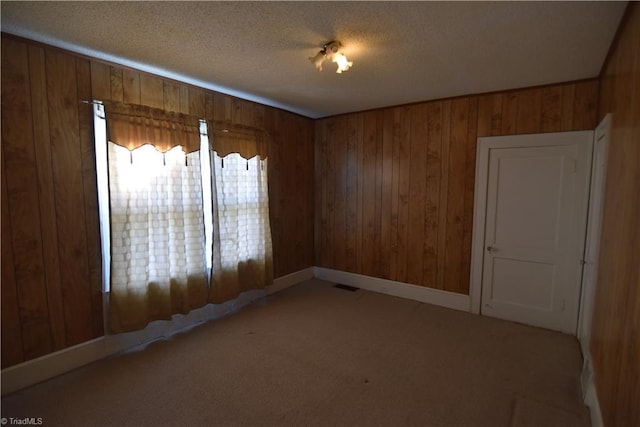 spare room with wooden walls, light colored carpet, and a textured ceiling