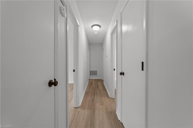 hallway featuring light wood-style floors, visible vents, and baseboards