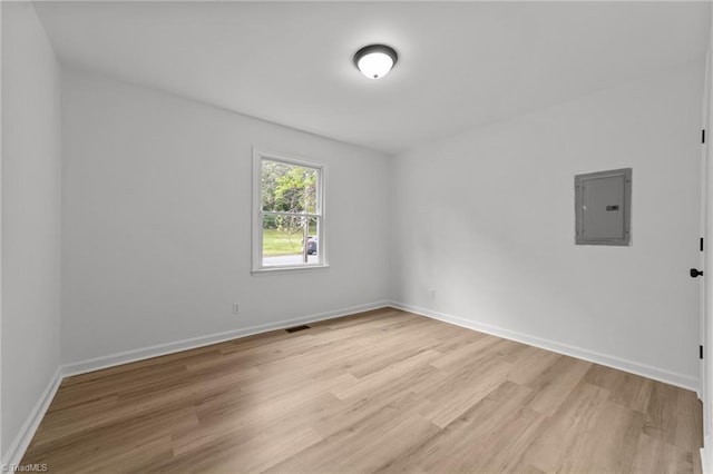 empty room with light wood-type flooring, electric panel, baseboards, and visible vents