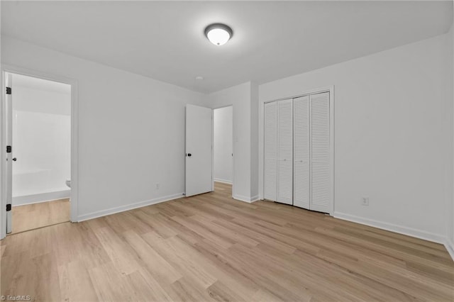 unfurnished bedroom with light wood finished floors, ensuite bath, baseboards, and a closet